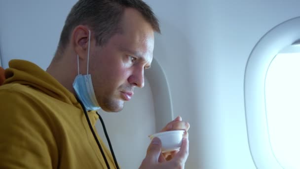 Un homme portant un masque médical mange assis dans un avion — Video