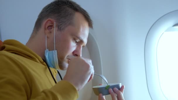 Mann mit medizinischer Maske isst im Flugzeug — Stockvideo