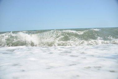 Denizdeki ortalama dalgalar kıyıya köpükle ulaşır ve bir gürültüyle kayalara çarpar.