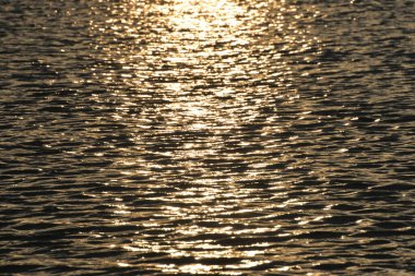 Gün batımında güzel bir göl, güneş ışınları suyu boyuyor ve küçük dalgalar altın, kırmızı, turuncu