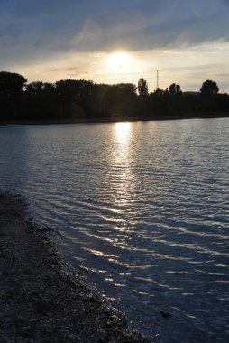 Gün batımında güzel bir göl, güneş ışınları suyu boyuyor ve küçük dalgalar altın, kırmızı, turuncu 