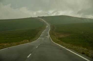 Yol yatağı düzensiz, sarmal, dağların ve kayalıkların arasından geçiyor. Bulutlar karanlık, alçak ve yağmurlu. Yol boyunca yoğun beyaz bir sis yayılıyor..