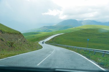 Yol yatağı düzensiz, sarmal, dağların ve kayalıkların arasından geçiyor. Bulutlar karanlık, alçak ve yağmurlu. Yol boyunca yoğun beyaz bir sis yayılıyor..