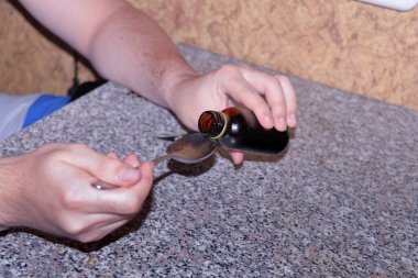 Adam kendine kaşığa ilaç dolduruyor, evde öksürük tedavisi görüyor.