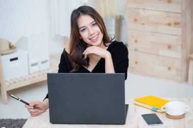 Güzel gülümseyen Asyalı kadın çevrimiçi eğitim servisinden öğreniyor, genç Asyalı kadın bilgisayar, dizüstü bilgisayar, not defteri ve akıllı telefon ile ödev yapıyor.