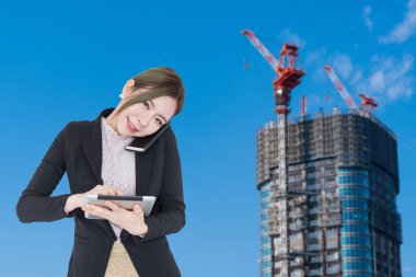Genç Asyalı iş kadını tablet akıllı telefon teknolojisi kullanıyor. Arkaplanda bina inşaatı ve kopyalama alanı var.