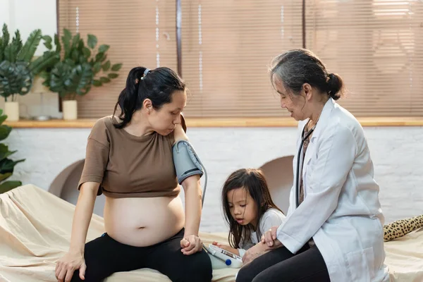 Senior Asiatisk Kvinnlig Läkare Hembesök För Ung Gravid Kvinna Patient Royaltyfria Stockfoton