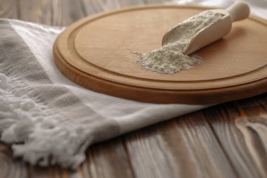 Ev yapımı ekmek için hazırlıklar. Pişirme için temel maddeler. Bir kesme tahtası üzerinde bir tahta kaşık un. Mutfak havlusu ve rustik ahşap masa