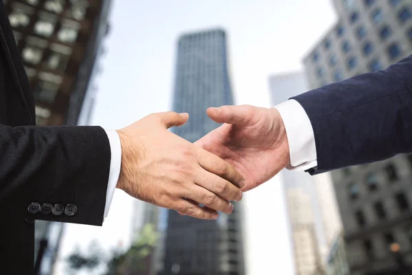 Handshake of two businessmen on the background of office building windows, partnership concept, close up