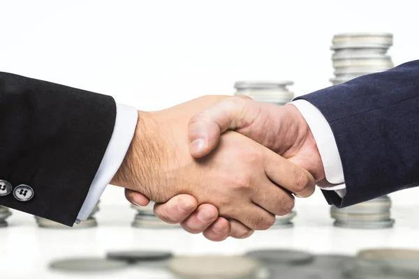 Два бизнесмена пожимают руки на фоне растущих пачек монет, зарабатывая деньги концепцию, крупным планом — стоковое фото