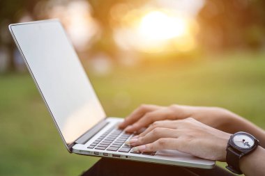 Günbatımı zaman parkta oturan ve dizüstü bilgisayar kullanan kadın kapatmak