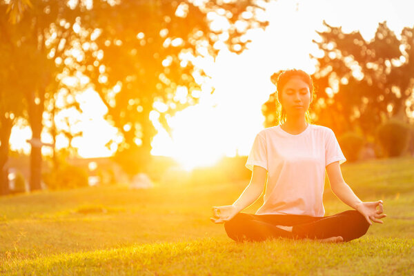 Pretty asian woman doing yoga exercises in the park with sunset lens flare effect. Used for relax and healthy concept