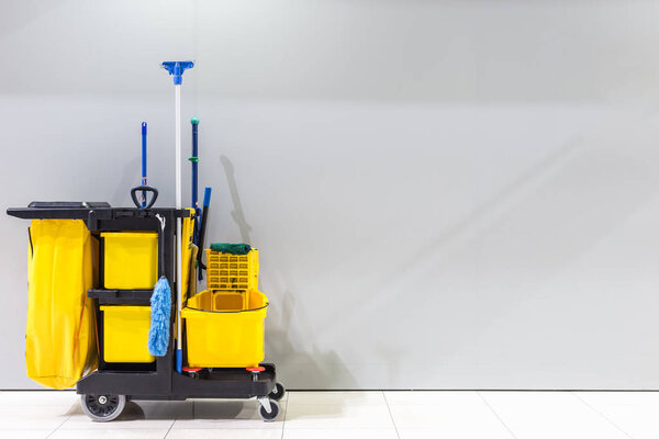 Yellow mop bucket and set of cleaning equipment and sign of men toilet on the wall in the airport