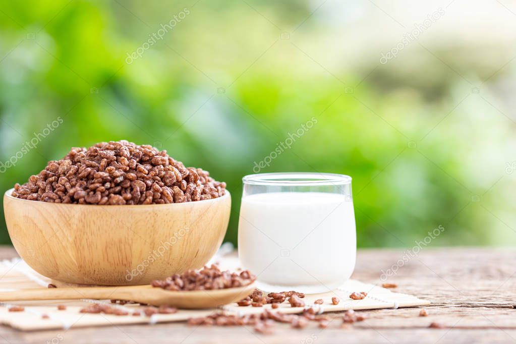 Breakfast cereal, Puffed rice with cocoa in bowl and glass of milk on wooden table with green blur space background for text or design. Food concept