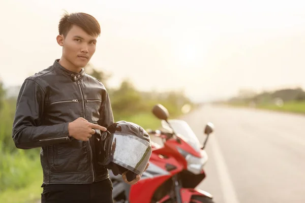 Schöner Motorradfahrer trägt Lederjacke und hält Helm auf — Stockfoto