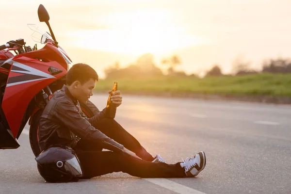 Motorradfahrer sitzt neben seinem Motorrad auf der Straße und trinkt — Stockfoto