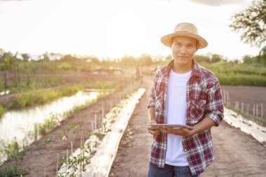 Asyalı akıllı çiftçi organik çiftliğinde tablet tutuyor. Technolog