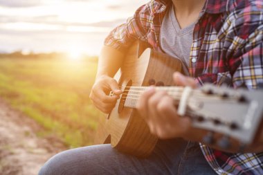 Gün batımında yeşil pirinç alanında gitar çalan Asyalı adam t