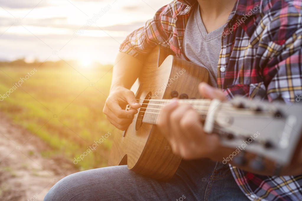 Asian man playing guitar at the green rice field in the sunset t