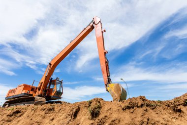 Büyük turuncu çizgili kazıcı işliyor ve toprağı kazıyor.