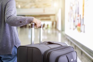 Genç turist havaalanında yürüyor ve bavullarını çekiyor.