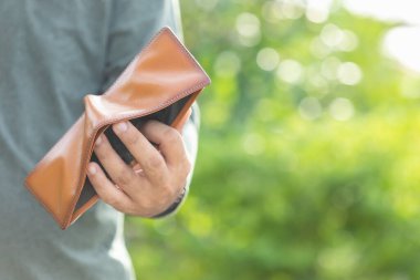 Asyalı adam boş cüzdan tutuyor. Para sorunu konsepti. Yeşil bulanık arkaplan ile açık havada çekim
