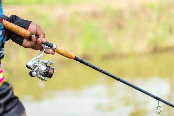 Close up fishing reel and rod in fisherman hand in a pond
