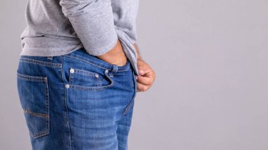 Kıymık ya da Tinea Cruris konsepti. Adam, gri arka planda pantolon stüdyosunun altını kaşıyarak çekim yapıyor.