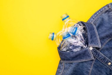 Giysi yapmak için plastik şişe teknolojisini geri dönüştür. Üst manzara eski su şişesi ve sarı arka planda mavi gömlek kotu.