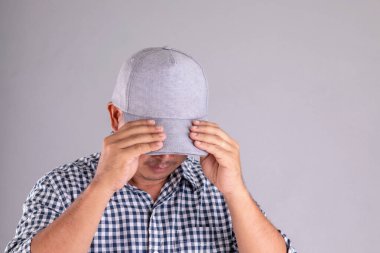 Gri şapkalı adamı kapatın ve yüzünü gri arka planda kameradan saklayın.