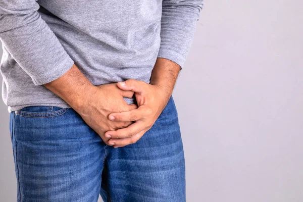 Pain on penis concept : Man use his hands to press on his penis on grey background