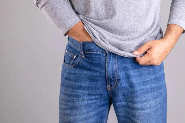 Kıymık ya da Tinea Cruris konsepti. Adam, gri arka planda pantolon stüdyosunun altını kaşıyarak çekim yapıyor.