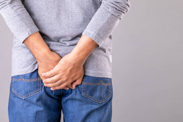 Закройте руку человека держа задней стороны на сером фоне: Концепция геморроя