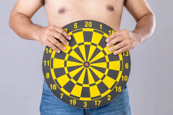 Fat people holding round yellow dartboard beside his belly position. Target of losing weight concept. Studio shot isolated on grey background