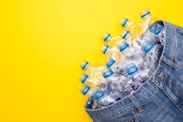 服を作るためのプラスチックボトルのリサイクル技術 黄色の背景に古い水ボトルと青のショートジーンズをトップビュー — ストック写真