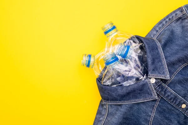 服を作るためのプラスチックボトルのリサイクル技術 黄色の背景に古い水ボトルと青のシャツジーンズをトップビュー — ストック写真