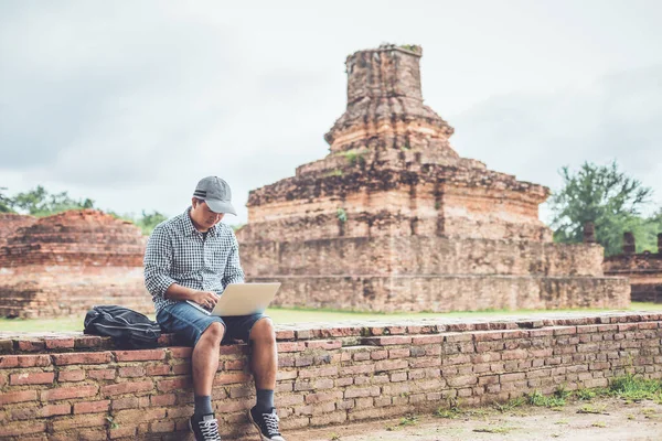 Asian tourist working and using laptop at Sukhothai historical park, Thailand. Vacation and holiday concept