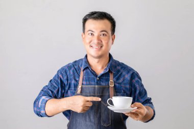 Kahveci üniformalı Asyalı bir portre elinde beyaz kahve fincanı ve sol üst fincanı gri arka planda izole edilmiş.