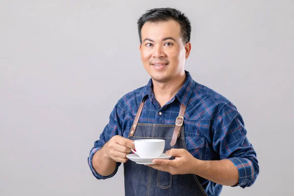 Portrait Asian man in barista uniform holding white coffee cup isolated on grey background