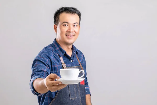 身穿巴里斯塔制服 手持灰色背景的白色咖啡杯的亚洲人的画像 — 图库照片