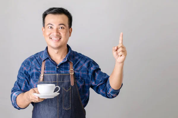 身穿巴里斯塔制服 手持白色咖啡杯的亚洲人的画像 左手指向上方 与灰色背景隔离 — 图库照片