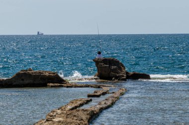 Güneşli bir günde Akdeniz 'de Akdeniz' de bir kaya oluşumunda balık tutan bir kişi..
