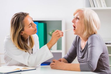 Kadın doktor ofisinde kıdemli onun hastanın boğaz inceliyor.