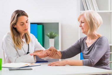 Kadın doktor ofisinde kıdemli onun hastanın bilek inceliyor.