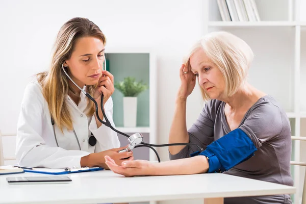 Kadın doktor doktor ofisinde kıdemli onun hasta için kan basıncı ölçme.
