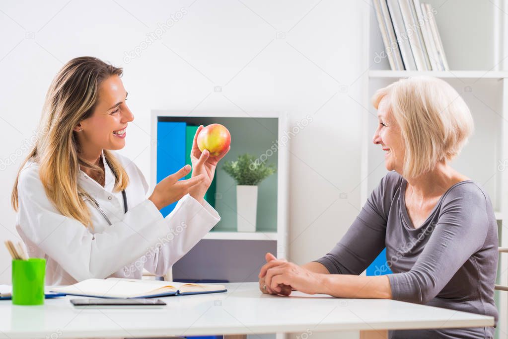 Female doctor is giving advice about eating healthy food to her senior woman patient .