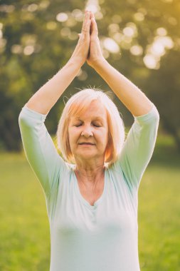 Kadın kıdemli doğada meditasyon sahiptir. Görüntü kasten tonda.