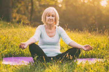 Kadın kıdemli doğada meditasyon sahiptir. Görüntü kasten tonda.
