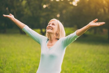 Kollarını doğada uzanmış ile kadın kıdemli sahiptir. Görüntü kasten tonda.