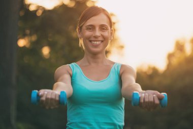 Güzel kadın doğada ağırlıkları ile egzersiz sahiptir. Görüntü kasten tonda.